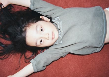 Child lying on a red surface wearing JEJEUNOSITY kidswear