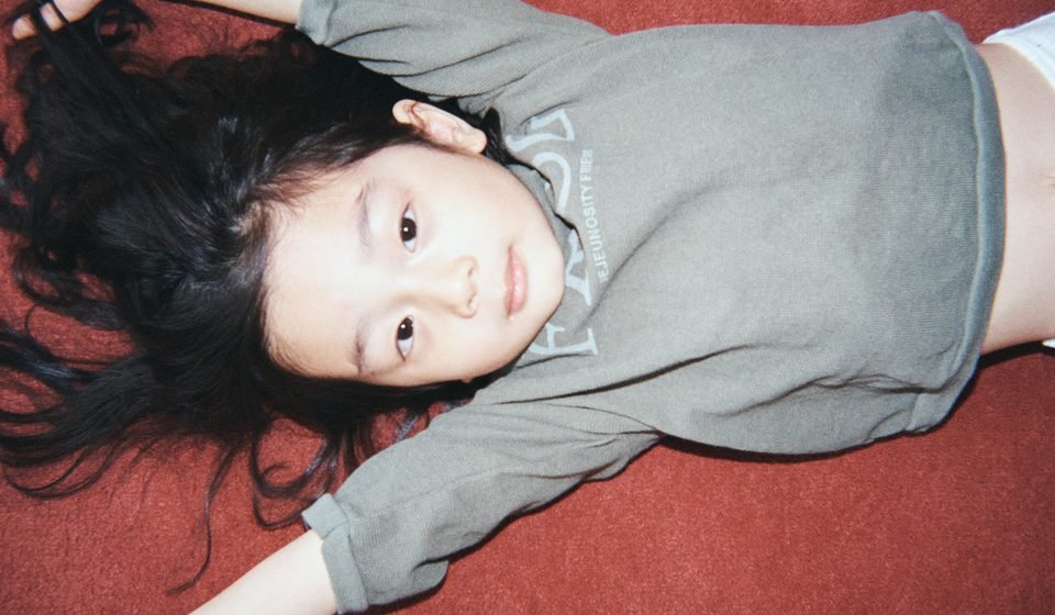 Child lying on a red surface wearing JEJEUNOSITY kidswear